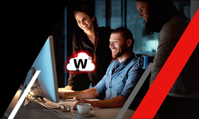 Uomo sorridente al computer con due persone alle sue spalle che guardano