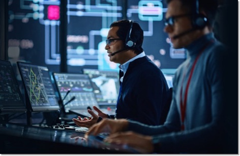 2 men with headsets working in a SOC with screens and projected code on the walls