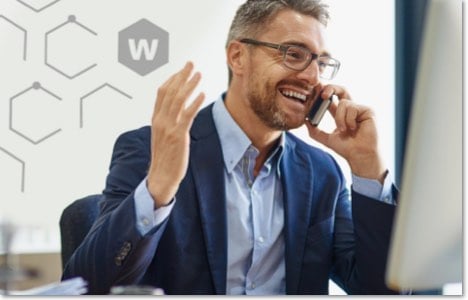 Man in a suit and glasses talking on the phone in front of his computer