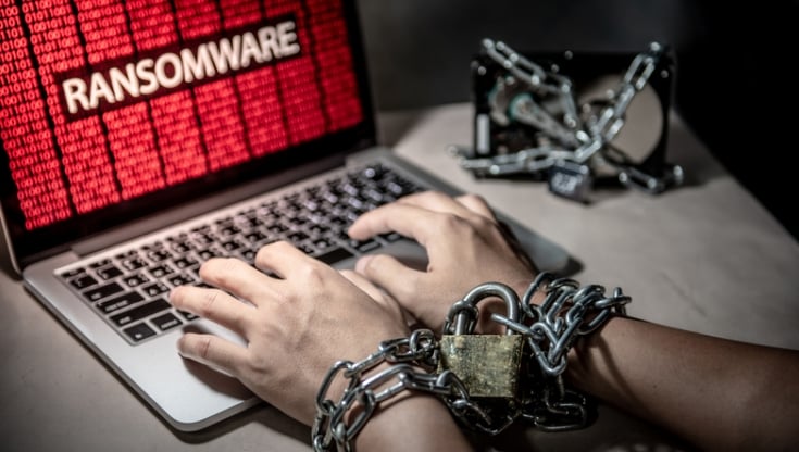 Hands chained with a padlock typing on a laptop showing a ransomware attack warning; symbolizing data encryption and cyber extortion.