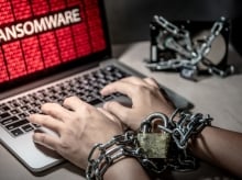 Hands chained with a padlock typing on a laptop showing a ransomware attack warning; symbolizing data encryption and cyber extortion.